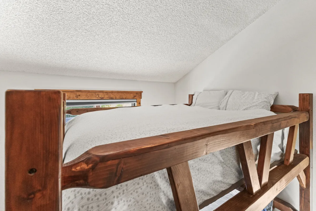This image features a lofted bed with a wooden frame and soft bedding, evoking a calm and peaceful retreat. The elevated sleeping arrangement is perfect for teens or singles seeking a touch of privacy within a group setting.