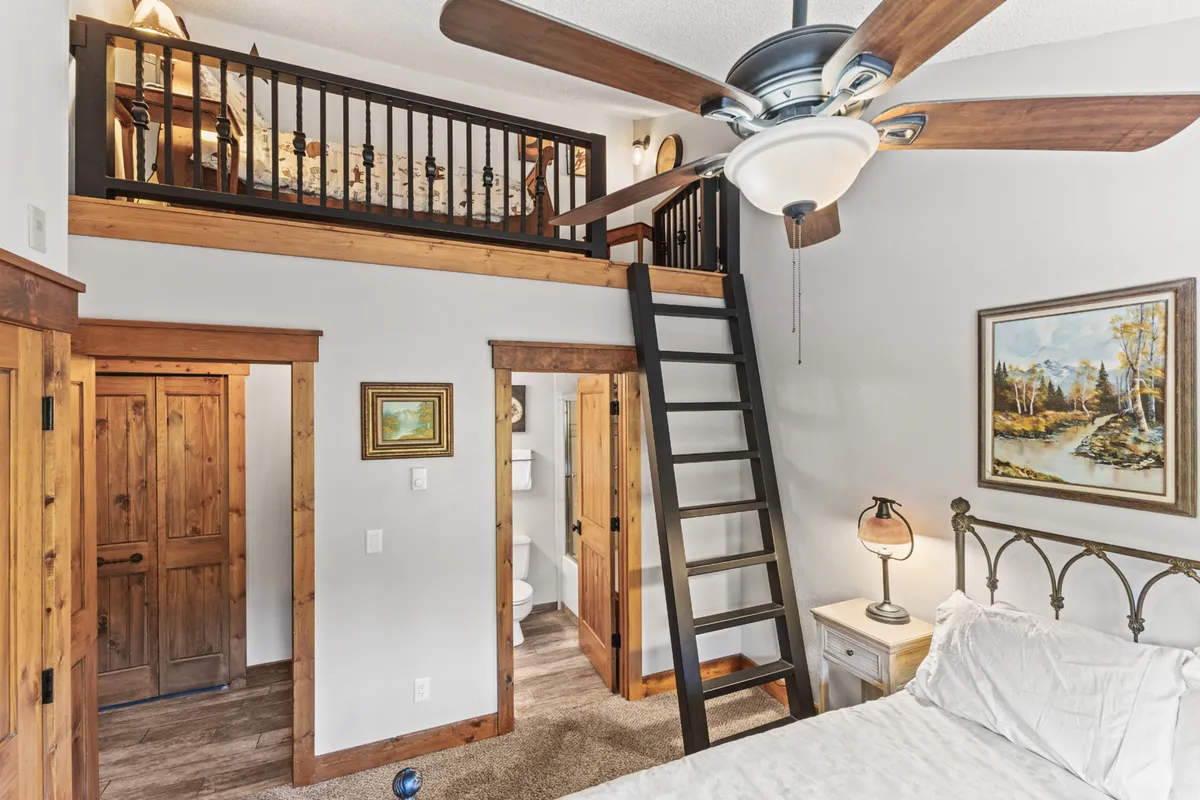 A warm and inviting loft area showcases a bed accessible by ladder, with soft lighting and thoughtful artwork. The space exudes coziness, making it an attractive choice for a child or a solo traveler seeking a private nook within the main level Queen suite.