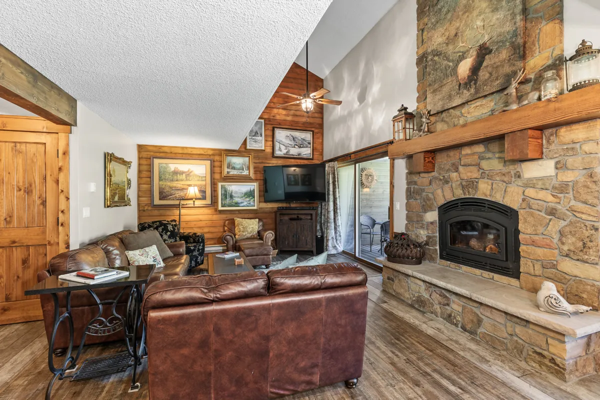 A cozy living space featuring a comfortable leather sofa, a robust stone fireplace, exposed wooden beams, and nature-inspired artwork. The atmosphere is warm and inviting, perfect for relaxing together after a day outdoors.
