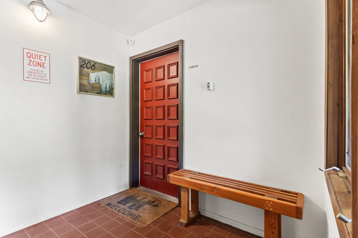 This image captures the inviting red door entrance of the condo, complete with a wooden bench, a welcome mat, and a 'quiet zone' sign. The scene suggests a calm and welcoming environment from the very first step, underscoring the property's commitment to peace and serenity.