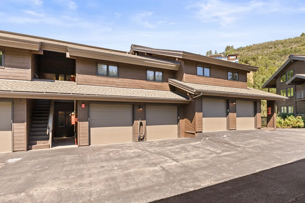 An inviting exterior view of the home featuring a wooden facade, garage doors, and a landscaped area, with the suggestion of sunset views from balconies and space for outdoor gatherings.