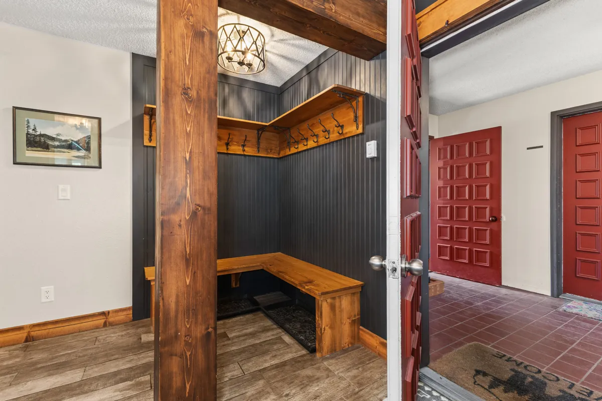 A warm and inviting mudroom with a wooden bench, coat hooks, an elegant chandelier, and red doors. This transitional space is designed for hanging coats, putting on shoes, or chatting with guests as you come and go from your mountain outings.