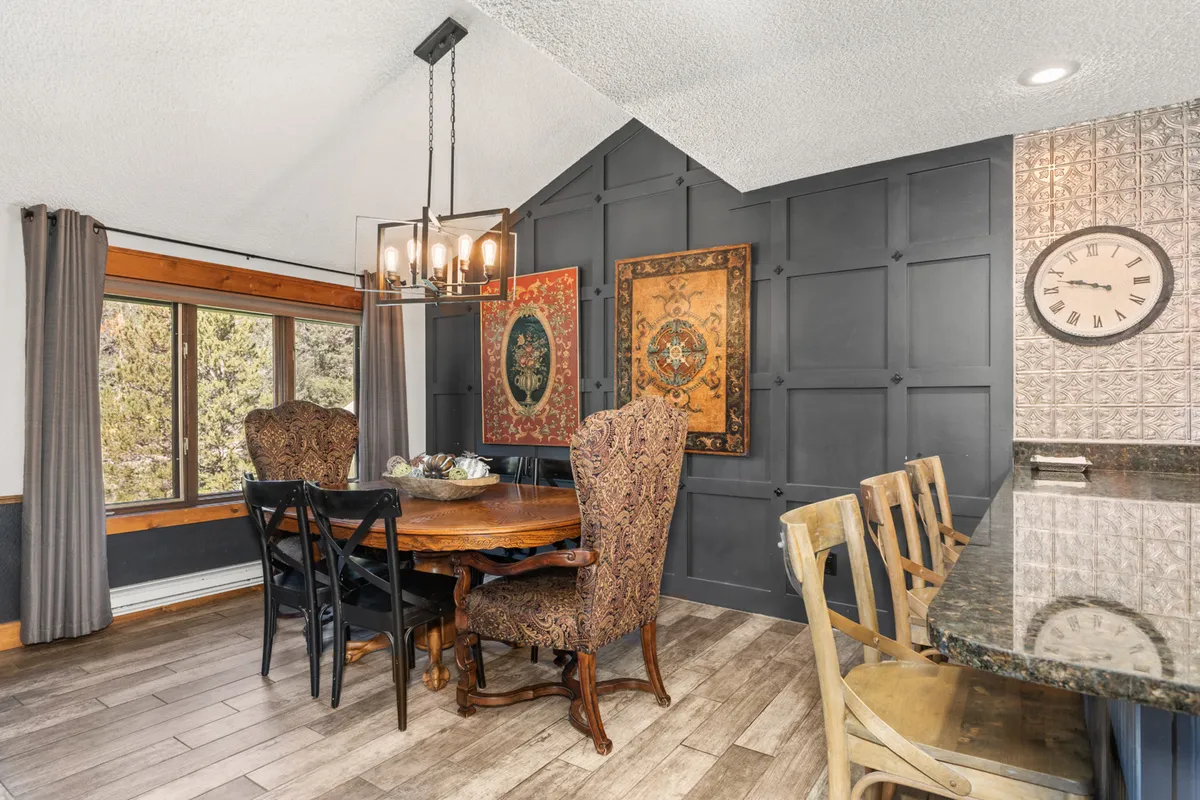 A warm, open-concept dining area with a wooden table, ornate chairs, a statement chandelier, and curated wall art. The space is designed for family-style meals and intimate group gatherings.