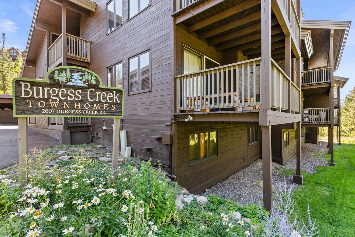 The exterior of the Burgess Creek Townhomes is captured here, with wooden balconies overlooking lush landscaping and visible signage. The atmosphere is serene and welcoming, suggesting relaxation after a day of outdoor adventure and a communal spirit ideal for group getaways or après-ski gatherings.