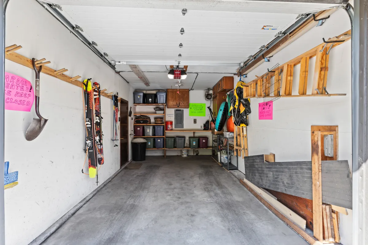 An organized garage area featuring tools and equipment neatly hung on the wall, colorful signs, and storage bins on shelves, illustrating ample gear storage for residents.