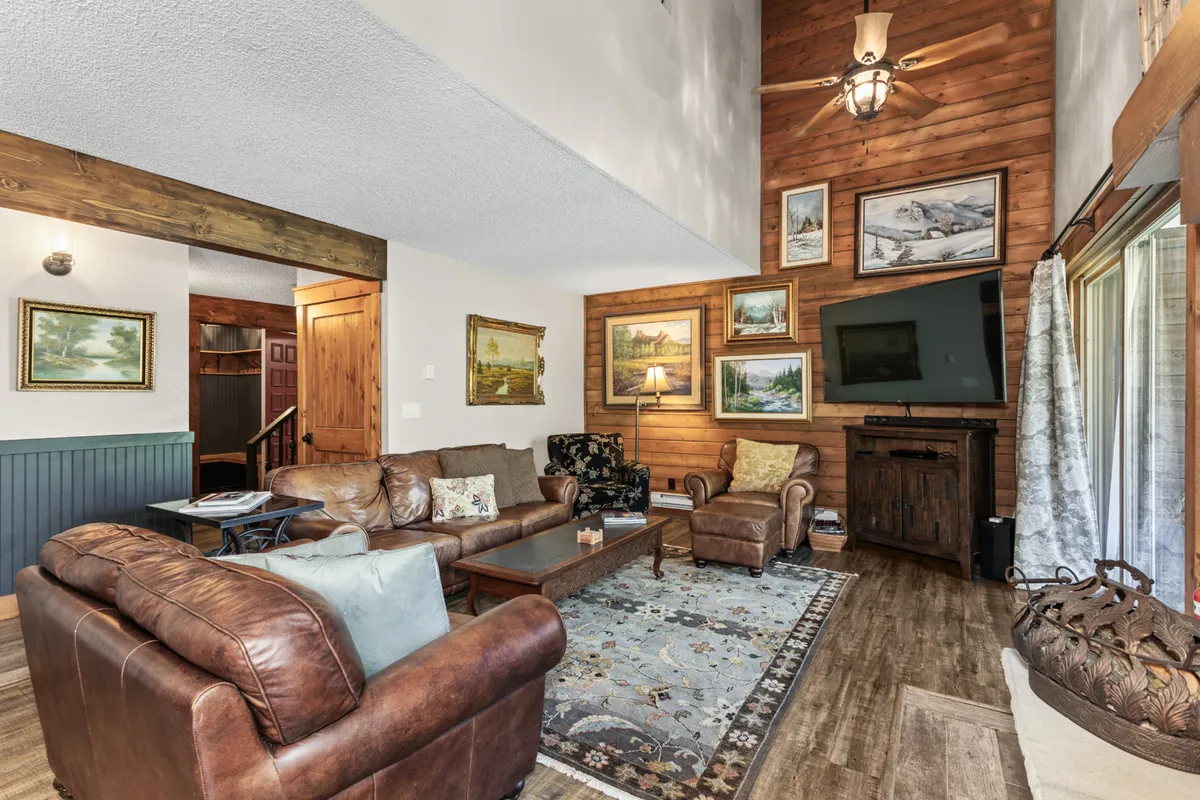 A cozy living area with leather sofas, a wooden coffee table, wall art, a flat-screen TV, and a rug, radiating an inviting and warm atmosphere ideal for relaxation and gathering.