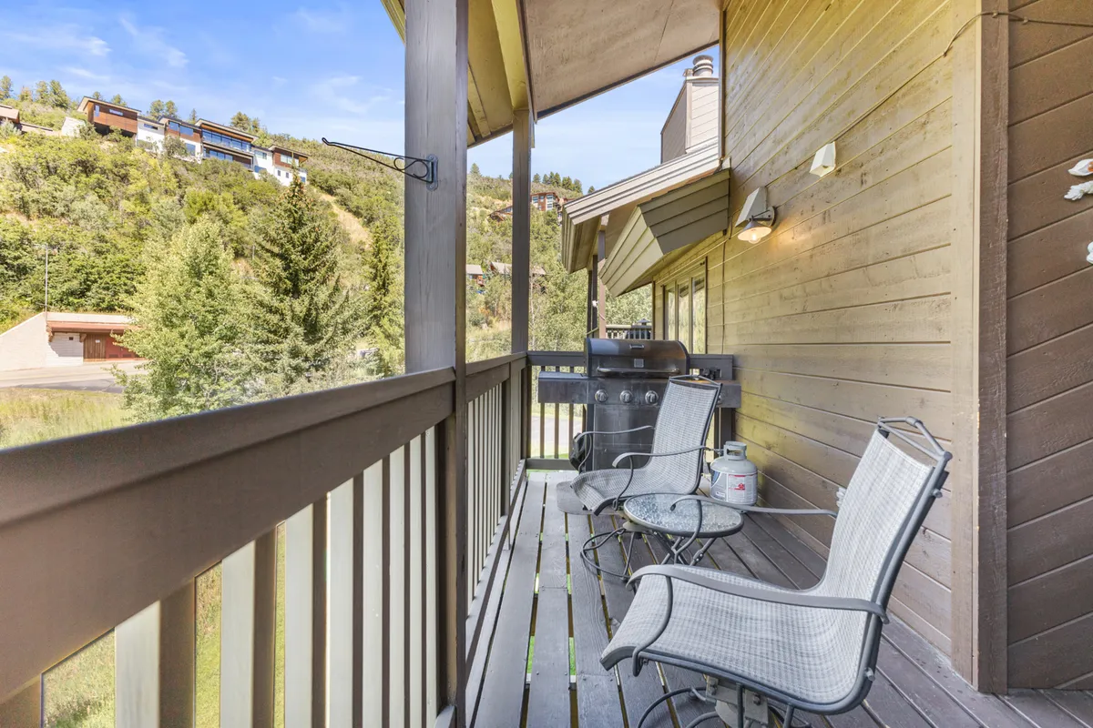 An inviting outdoor deck with comfortable chairs, a small table, and a grill, overlooking a scenic natural view. The space is designed for outdoor dining, morning coffee, and evening gatherings, all set against a tranquil backdrop.