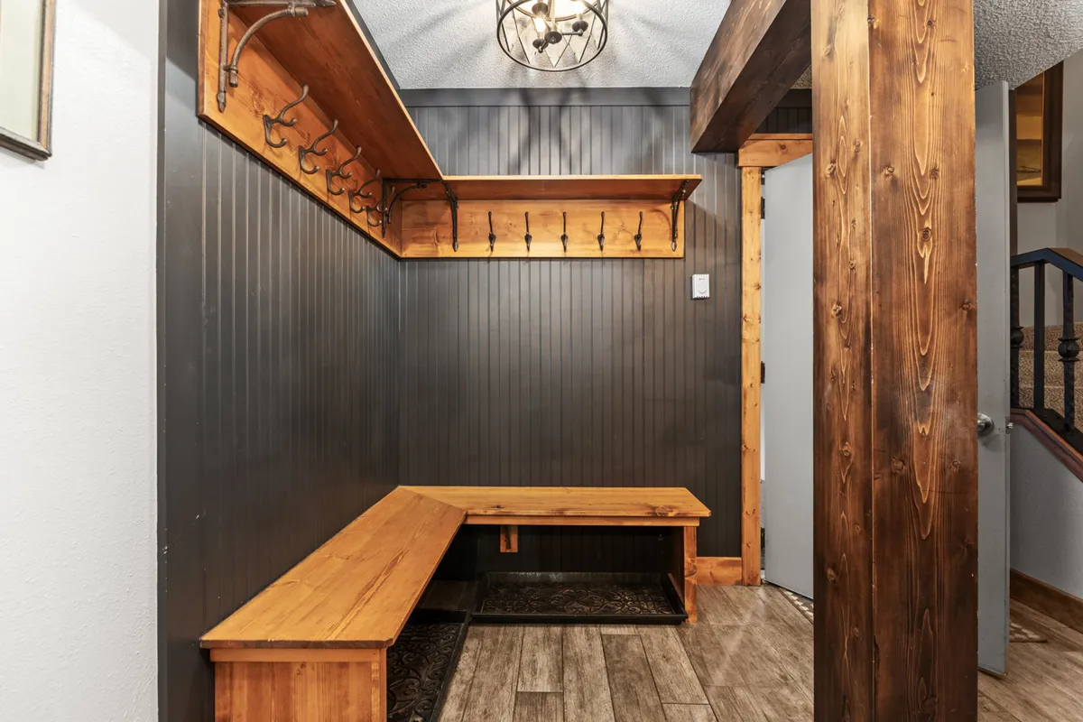 A cozy entryway featuring a wooden bench, a hook rack for coats, and a chandelier overhead. The natural wood tones and warm lighting create a welcoming first impression, inviting guests to pause and transition from the outdoors into a comfortable retreat.