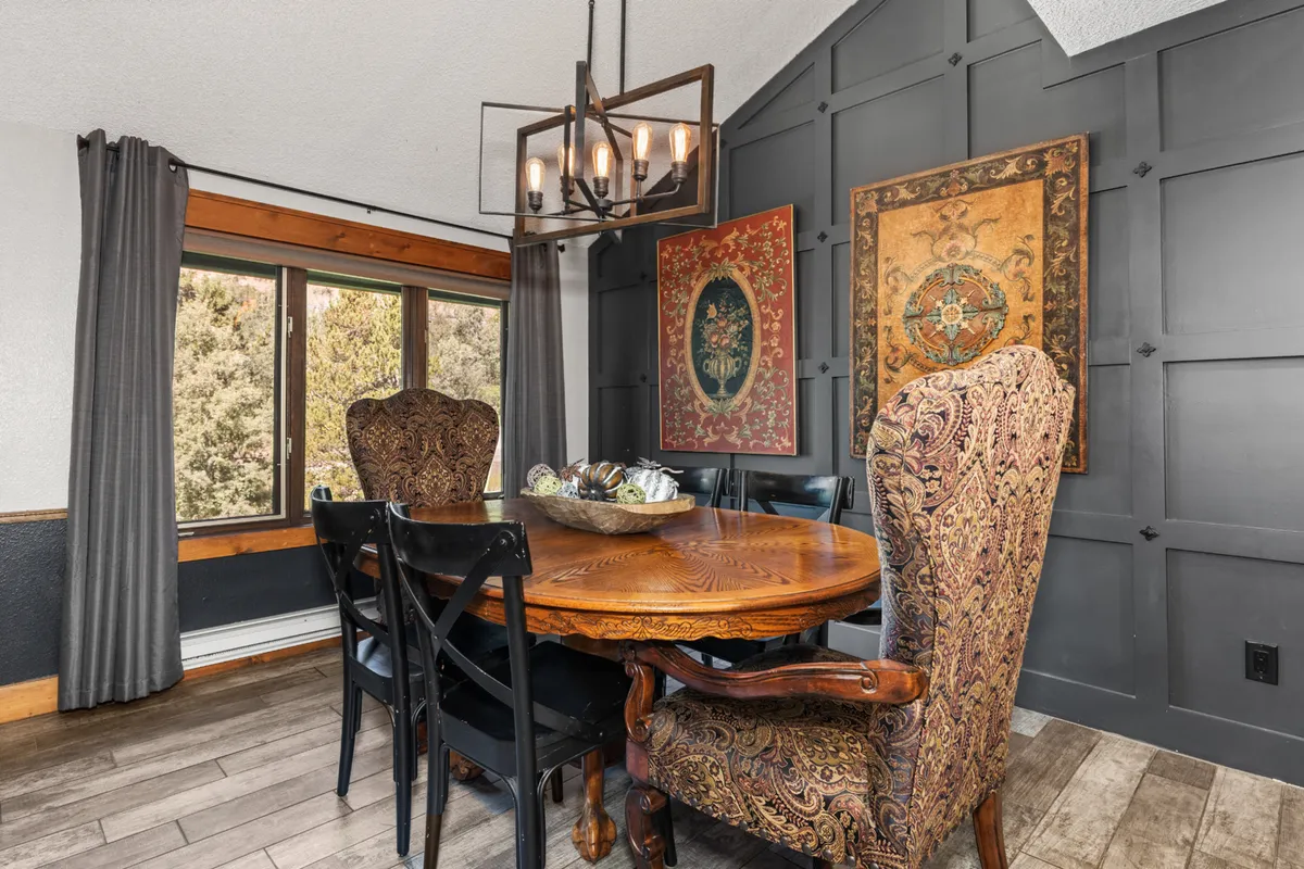 A sophisticated dining area with an ornate dining table, elegant chandeliers, wall art, and generously sized windows that offer views and fill the room with natural light.