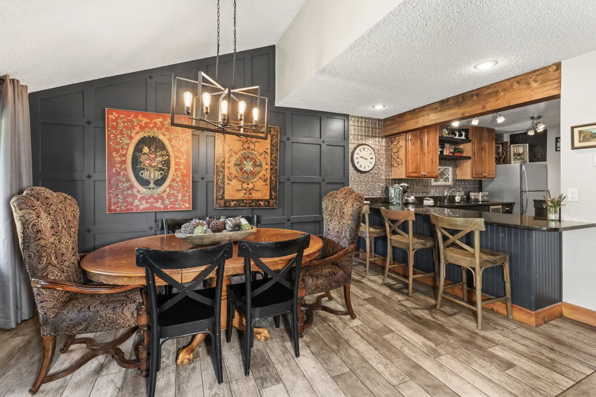 A spacious and cozy dining area with a large dining table under an elegant chandelier. Wall art adds interest, and a nearby kitchen bar area is visible, encouraging easy flow for social gatherings and meals.