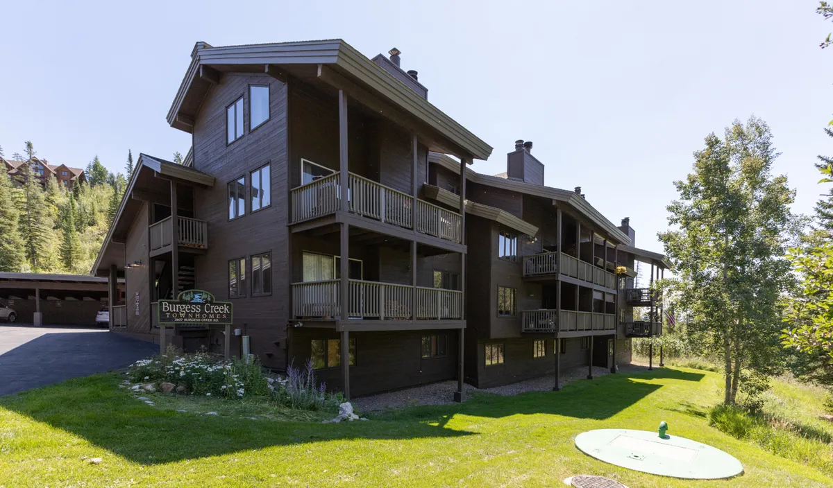This image displays a three-story building with prominent balconies and clear signage, set against a backdrop that hints at mountain scenery. The scene conveys a sense of connection to the outdoors and easy access to surrounding activities, with balconies that invite residents to take in the views and the environment.
