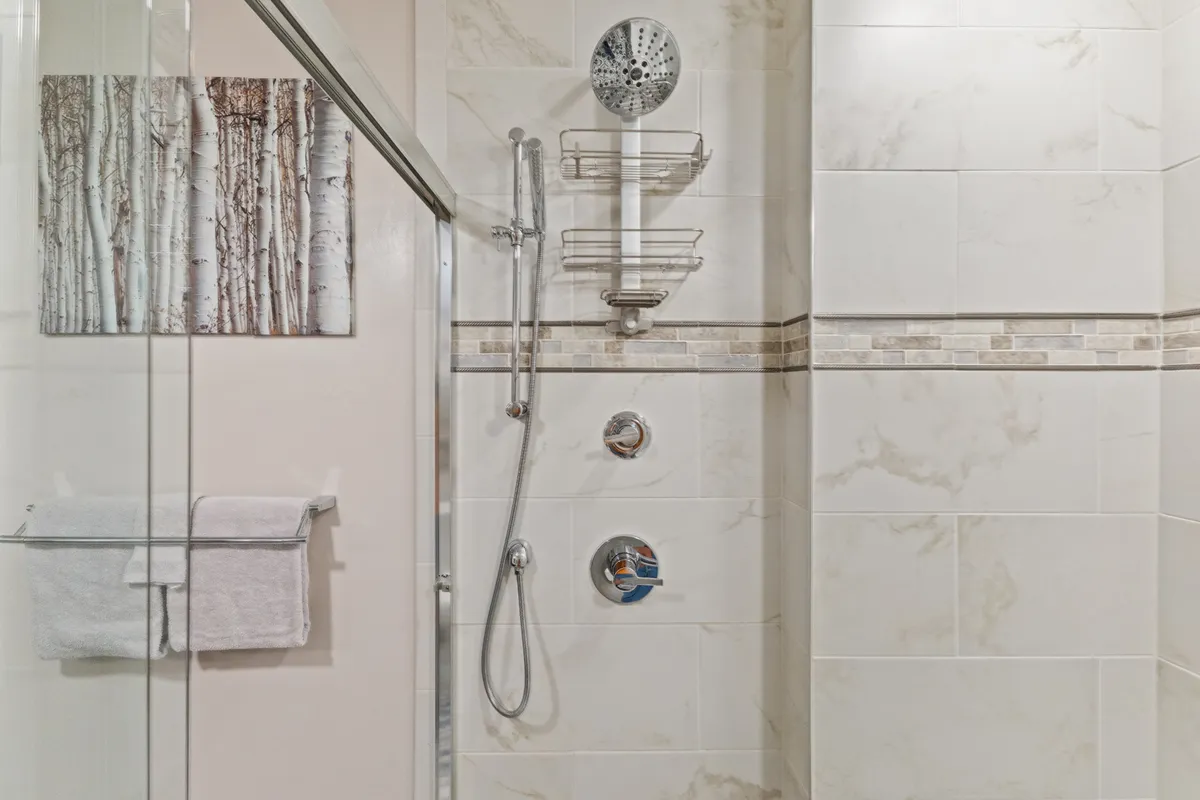 A modern bathroom with a rain showerhead, decorative wall art, and elegant tilework, evoking a sense of calm and luxury for self-care routines.